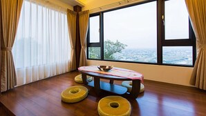 A room with a wooden floor, a round table with a bowl, and large windows with curtains. - Moonstone Bed and Breakfast (Sanxing)