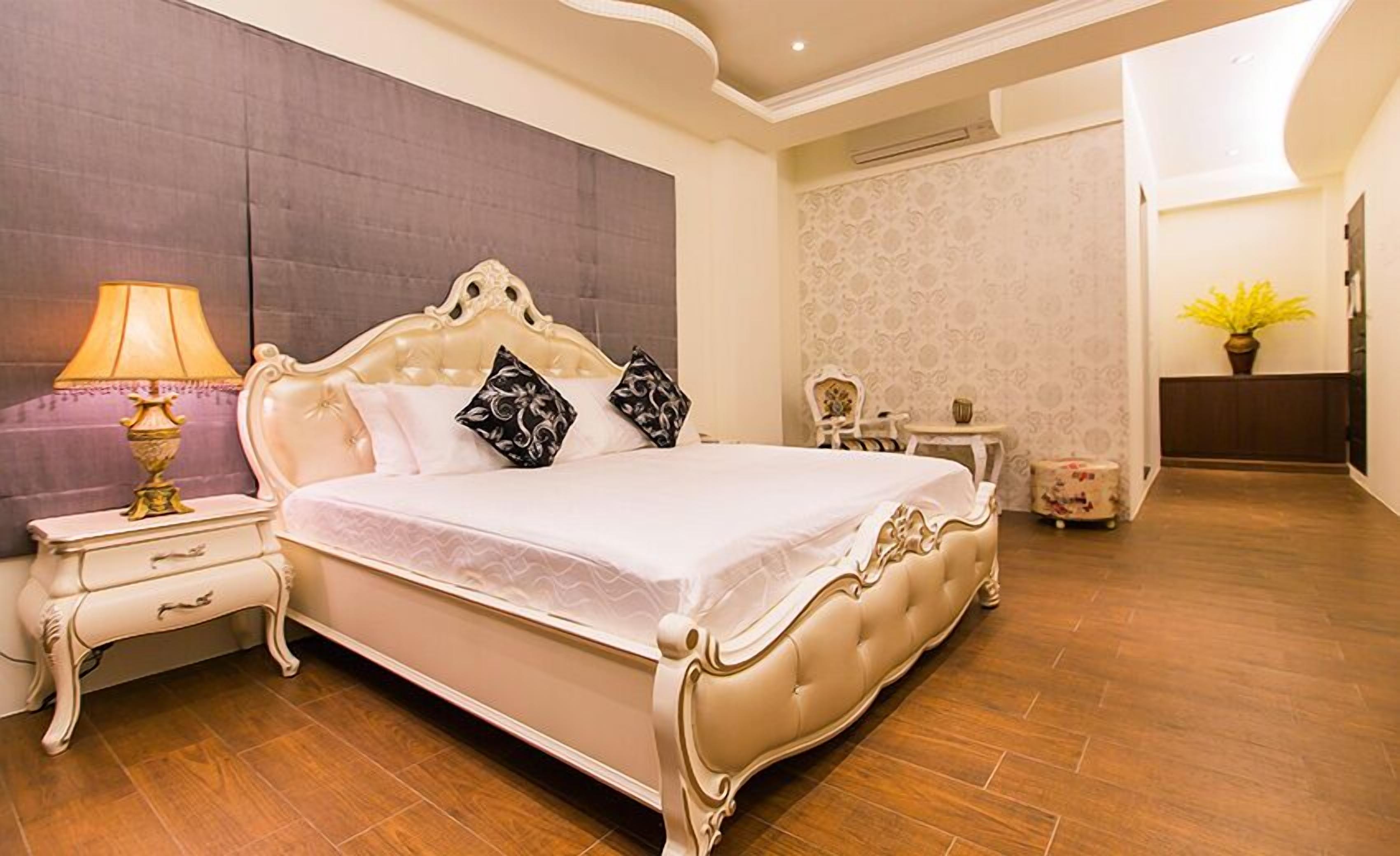 A spacious bedroom with a large bed, a bedside table, a lamp, and a small side table.