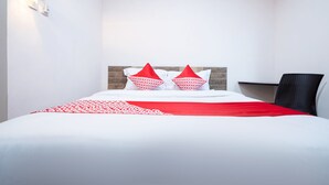 A hotel room with a bed, two pillows, a red and white bedspread, a wooden headboard, a black chair, and a wall-mounted light fixture. - Hotel O Art Guest House Syariah (Yogyakarta)