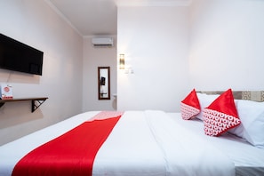 A hotel room with a bed, red and white pillows, a flat-screen TV, a shelf, a mirror, and an air conditioning unit. - Hotel O Art Guest House Syariah (Yogyakarta)