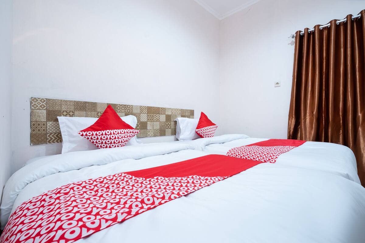 A neatly made bed with white and red bedding, a patterned headboard, and brown curtains.