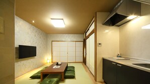 A traditional Japanese room with tatami flooring, a low table with cushions, a sliding shoji screen, and a modern kitchen with a sink and stove. - Asana-Yuuna (Kyoto)