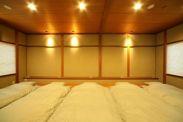 Three beds are aligned in a traditional Japanese-style room with wooden paneling and recessed lighting.