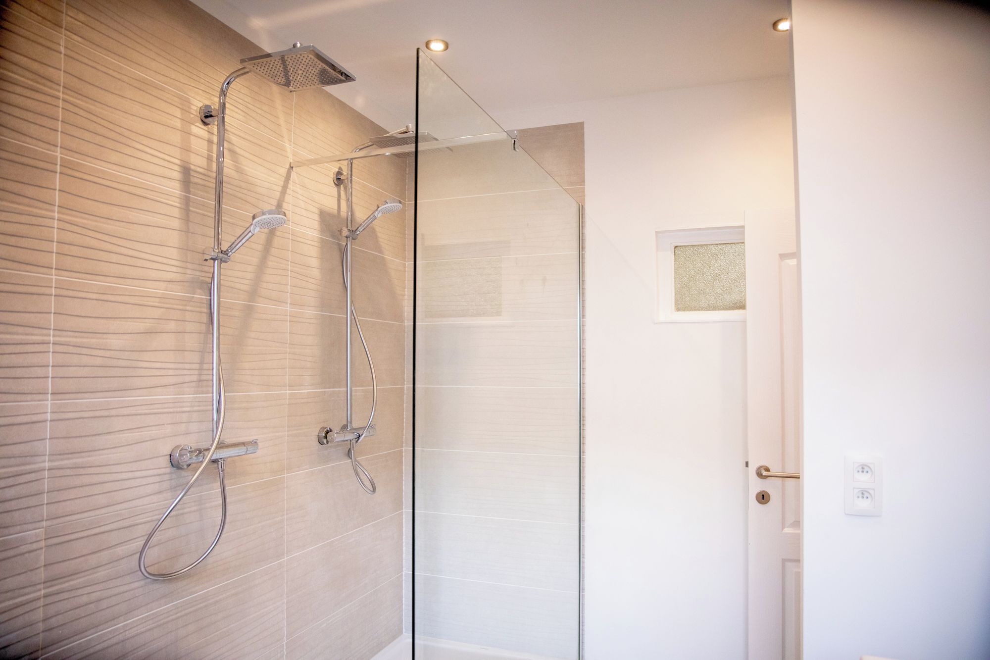 Ein modernes Badezimmer mit Duschkabine aus Glas, einem hängenden Handtuchhalter und einer Tür mit kleinem Fenster.