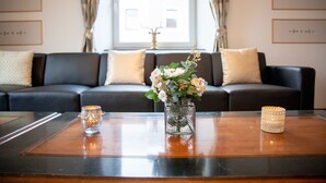 Una sala de estar moderna con un sofá de cuero oscuro, un florero de cristal con flores y una vela sobre una mesa de centro de madera.