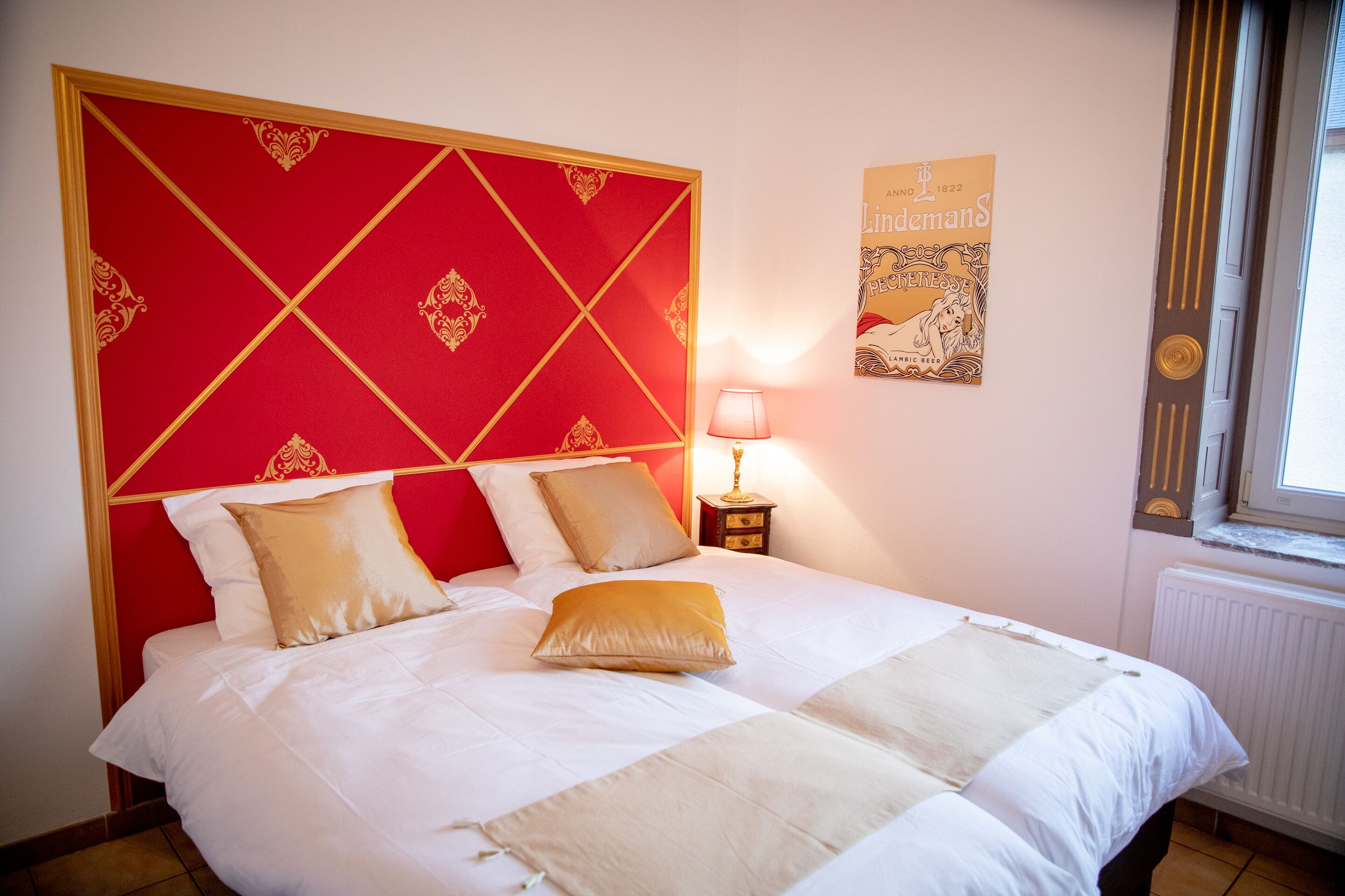 A neatly made bed with a red headboard, white bedding, and a lamp on a bedside table.
