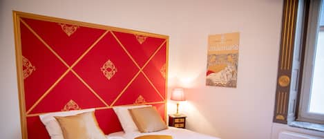 A neatly made bed with a red headboard, white bedding, and a lamp on a bedside table.