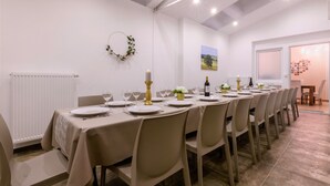 Un comedor con una larga mesa dispuesta para una comida, paredes blancas, una guirnalda y una ventana con vistas.