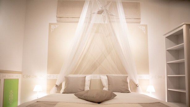 Una cama bien hecha con dosel, dos lámparas de noche y un panel verde en la pared izquierda.