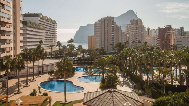 Un hôtel doté de plusieurs piscines, de palmiers et surplombant un paysage montagneux.