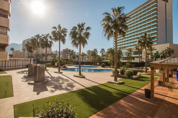 A courtyard with a swimming pool, palm trees, and a large hotel building in the background.