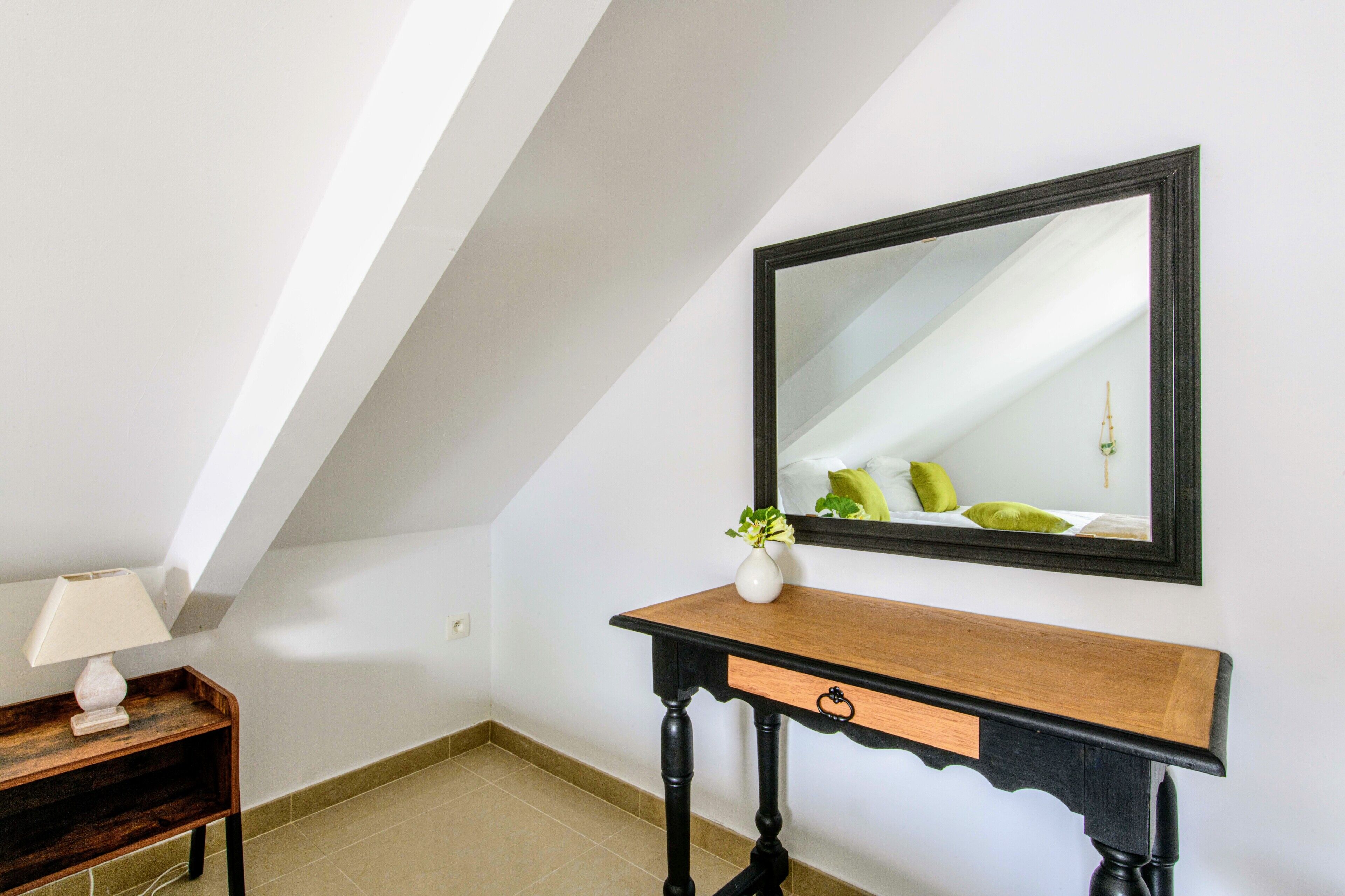 Une pièce comprenant une console en bois, un vase blanc avec une plante et un grand miroir au mur.