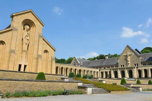 Un edificio histórico con una estatua destacada, una serie de arcos y una escalera de piedra que conduce a la entrada.