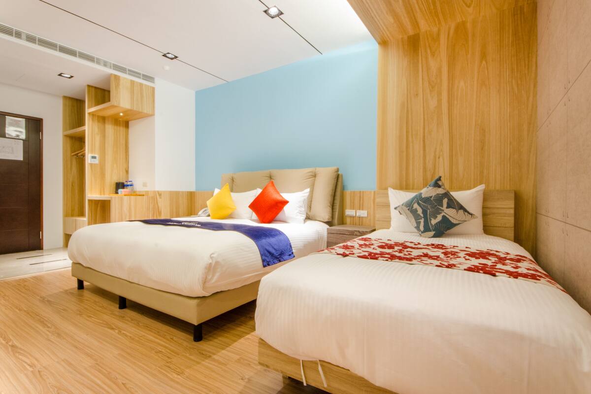 A modern hotel room with two beds, wooden paneling, and a blue accent wall.