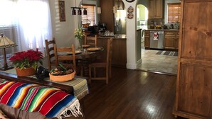 A dining area with a wooden table, chairs, and a colorful woven bench. There is a kitchen visible in the background with wooden cabinets and a refrigerator. - Beautiful Private Home in Long Beach near Convention Center and Queen Mary (Long Beach)