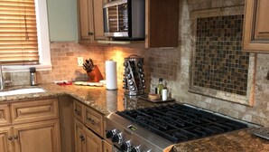 A kitchen with wooden cabinets, a stainless steel stove, a microwave, and a tiled backsplash. - Beautiful Private Home in Long Beach near Convention Center and Queen Mary (Long Beach)