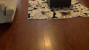 Ein Wohnzimmer mit einem beigen Sofa, einem dunklen Ottomanen und einem Teppich mit Blumenmuster.