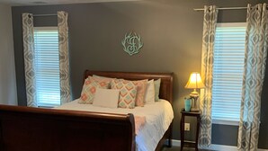 Ein Schlafzimmer mit einem hölzernen Bett, einem Deckenventilator, einem Nachttisch mit Lampe und gemusterten Vorhängen.