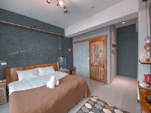 A modern bedroom with a large bed, a wooden door, and a small side table.