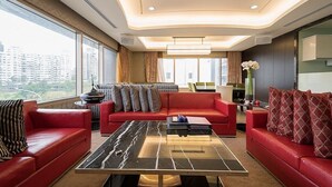 Ein modernes Hotelzimmer mit einer roten Sofagarnitur, einem schwarzen Marmortisch und großen Fenstern mit Blick auf die Stadt.