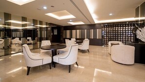 Eine moderne Lobby mit rundem Tisch und weiß gepolsterten Stühlen, einer Glaswand und einer Wand mit Muster und einer dekorativen Skulptur.