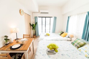 A hotel room with two beds, a dining table, and a small kitchen area.