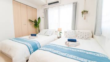 A hotel room with two beds, a large window with curtains, a potted plant, and an air conditioning unit.