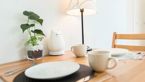 Une table à manger en bois, sur laquelle se trouvent une assiette blanche, une tasse, une petite plante en pot, une lampe en forme de chat et un set de table noir.