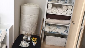 Une petite pièce avec une table noire, une étagère blanche où sont pliées des serviettes et un matelas blanc.