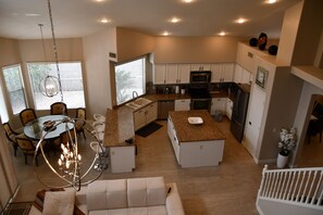 A modern kitchen with white cabinets, a dining area with a glass table, and a living room with a white sofa.