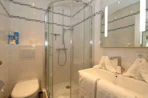 Ein modernes Badezimmer mit einer gläsernen Duschkabine, einer weißen Toilette und einem Waschbecken mit Spiegel.
