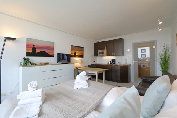 A modern hotel room with a bed, a desk, a television, a microwave, and a view of the cityscape.
