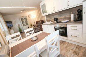 A modern kitchen with white cabinetry, a central island, and a built-in oven. - Greetsiel - Spacious apartment on the ground floor (Greetsiel)