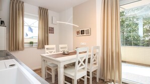 Une cuisine moderne avec des meubles blancs, une table à manger avec quatre chaises et une grande fenêtre avec des rideaux.