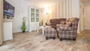 Un salon avec un canapé marron, un pouf à carreaux, un meuble blanc et une horloge au mur.