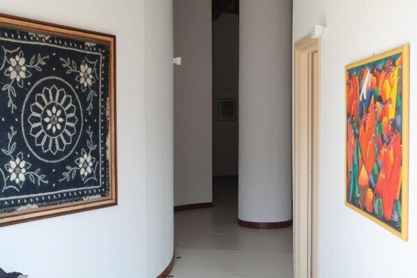 A hallway with a patterned tapestry on the left and a colorful painting on the right.