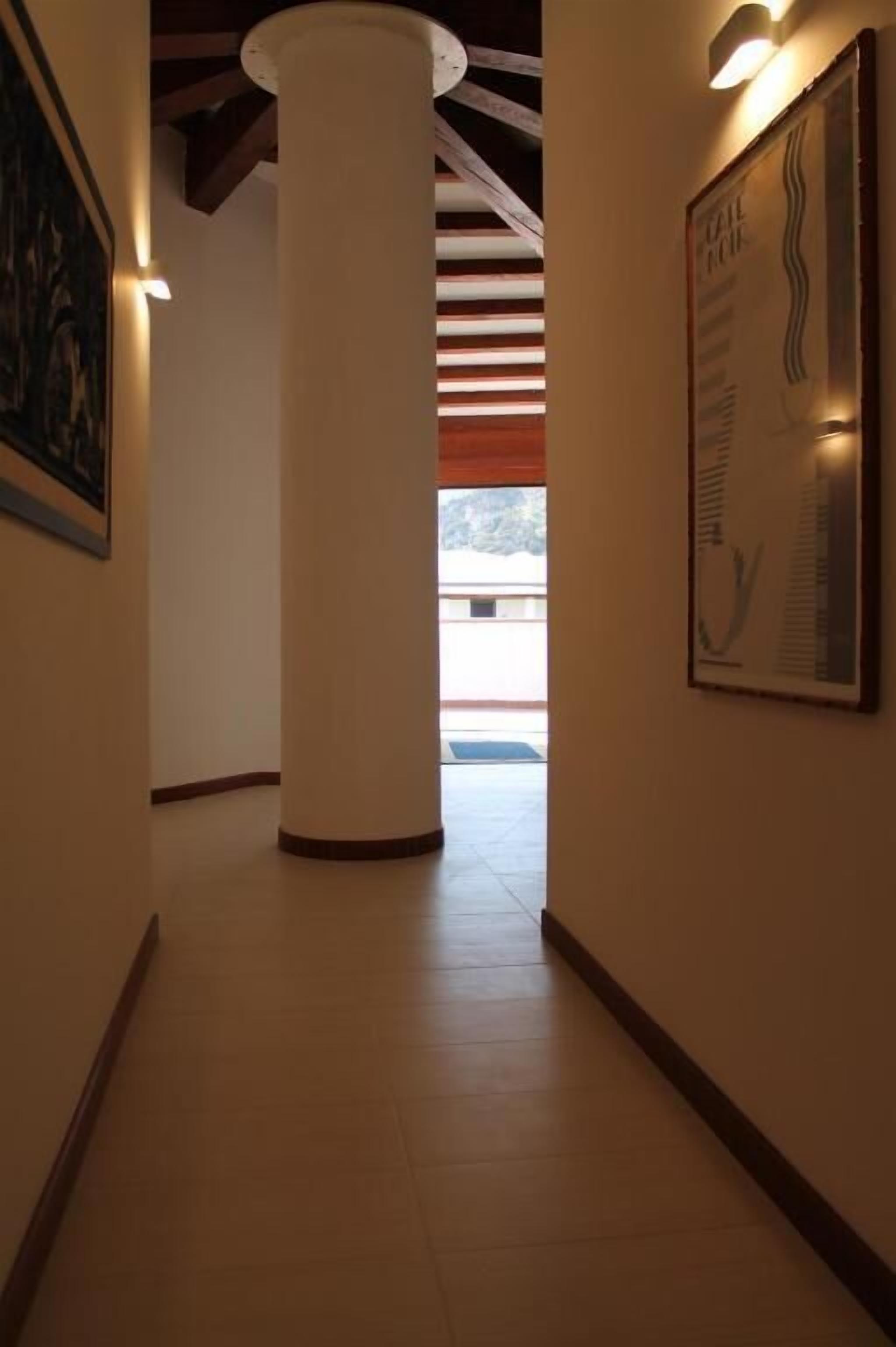 A hallway with a large white pillar, a framed informational poster, and a view of the outside.