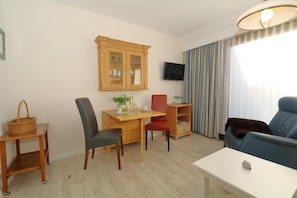 A living room with a dining table, chairs, a TV mounted on the wall, a sofa, and a window with curtains.