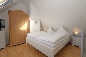 Ein Schlafzimmer mit einem Holfischschrank, einem Bett mit weißer Bettwäsche, zwei Nachttischen mit Lampen und einem gerahmten Bild an der Wand.