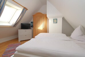 Ein Schlafzimmer mit schrägen Wänden, einem Bett, einem Nachttisch, einem Fernseher und einem Fenster mit Vorhängen.