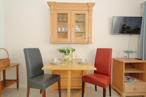 Ein Essbereich mit Holztisch, zwei Stühlen, einer Vitrine und einem Fernseher an der Wand.