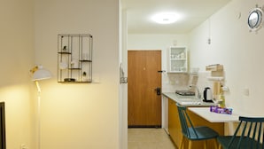 A compact kitchen with a wooden door, a white countertop, and two green chairs. - Stylish flat at Rothschild boulevard (Tel Aviv)