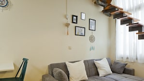 A living room with a grey sofa, a teal chair, and a white table. There are wall-mounted pictures and a dreamcatcher. - Stylish flat at Rothschild boulevard (Tel Aviv)