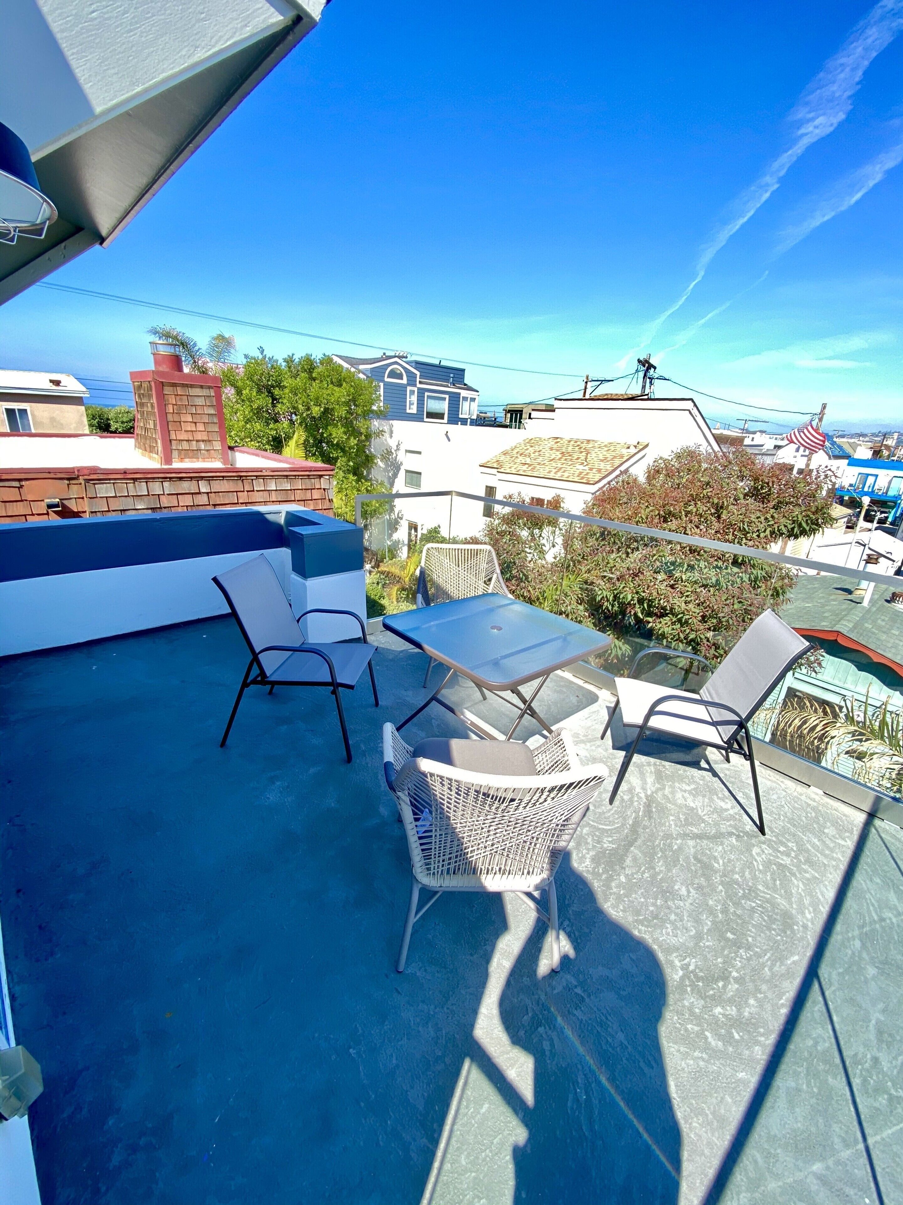 A rooftop patio with a table and chairs, overlooking a residential area with houses and a clear blue sky.