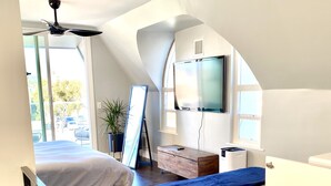 A modern bedroom with two beds, a ceiling fan, a TV, and a large window.