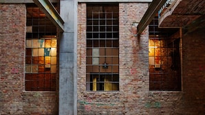 Vista interior de un edificio con paredes de ladrillo, barandales de metal y varias ventanas con rejas metálicas.