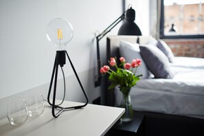 Una habitación moderna con escritorio, lámpara, un jarrón con flores y una cama.