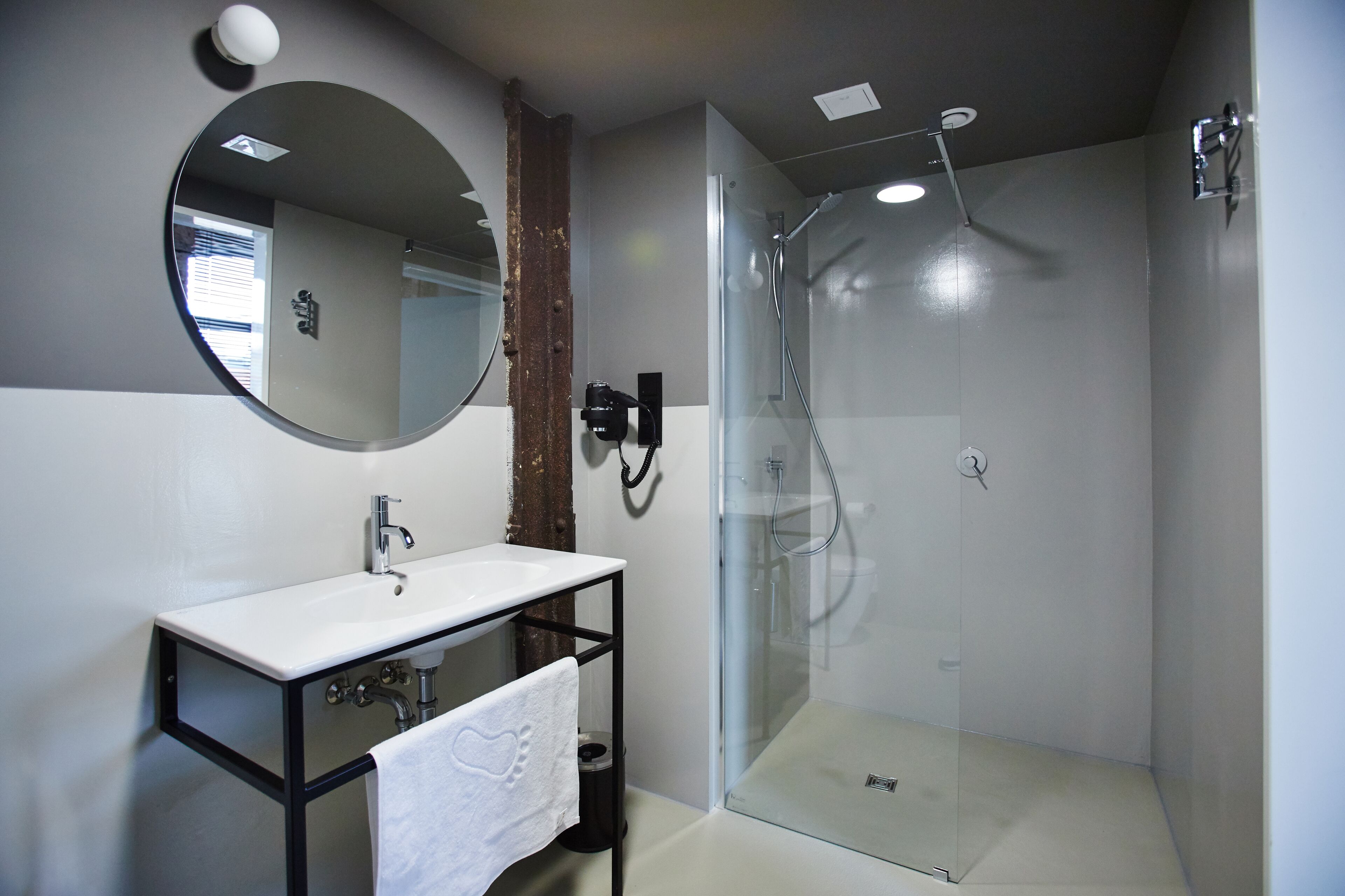 A modern bathroom with a glass-enclosed shower, a white sink, and a round mirror.