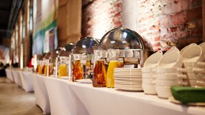 Una barra de buffet con diversos recipientes de comida y bebida, platos y tazones dispuestos sobre una mesa.