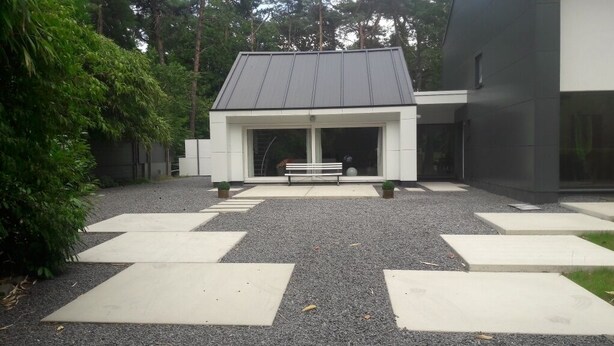 A modern building with a sloped roof, a bench in front, and a gravel pathway leading to the entrance. - B&B Golf Schilde (Schilde)